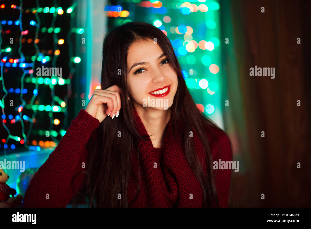 Picture of happy cheerful beautiful girl whit pretty white smile in studio with Christmas lights. Pretty smiling girl on colorful background with lights. Closeup portrait of nice girl with long hair. Stock Photo