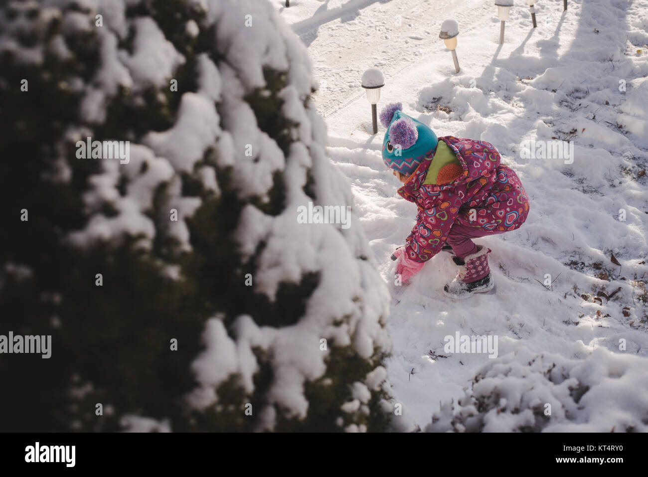 A toddler girl wearing a colorful coat plays in the snow Stock Photo ...