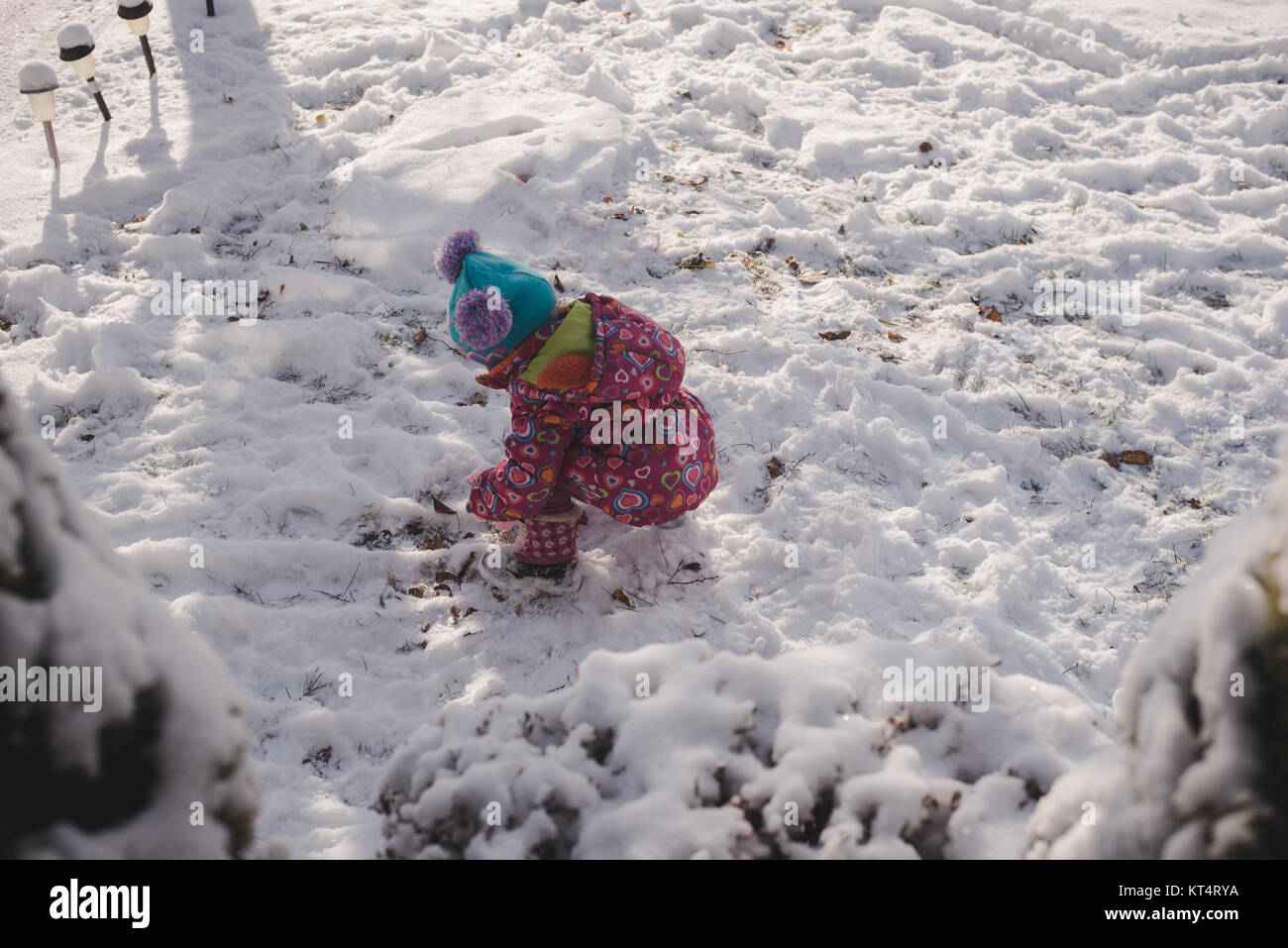 A toddler girl wearing a colorful coat plays in the snow Stock Photo ...