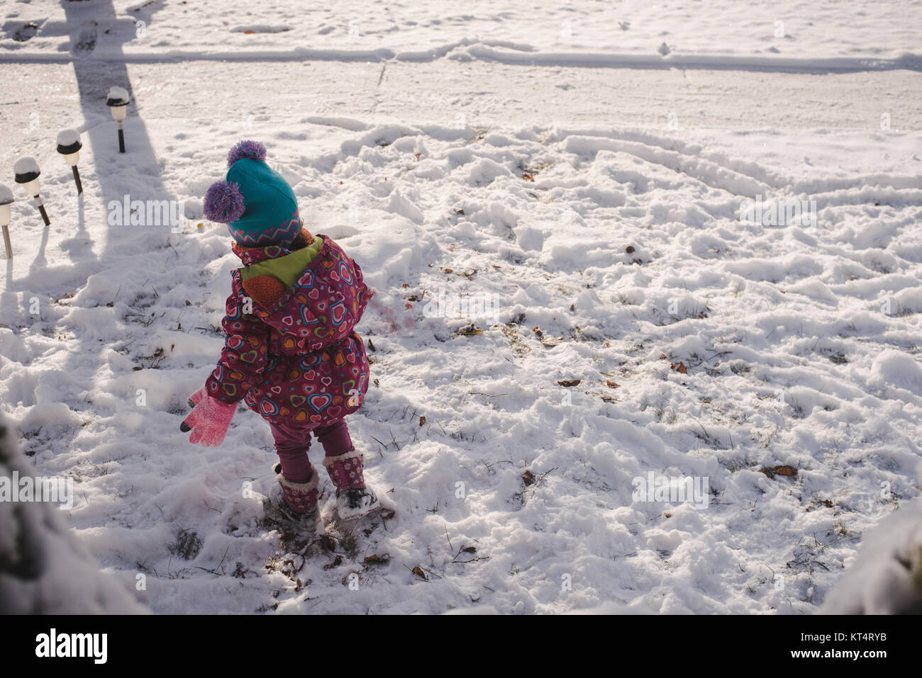 A toddler girl wearing a colorful coat plays in the snow Stock Photo ...