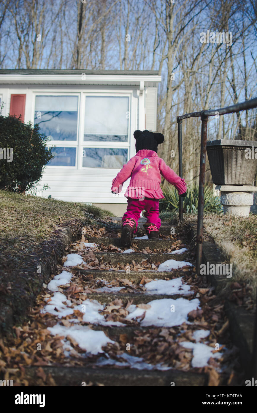 A child climbs up a flight of stone stairs wearing a sweater during the winter Stock Photo