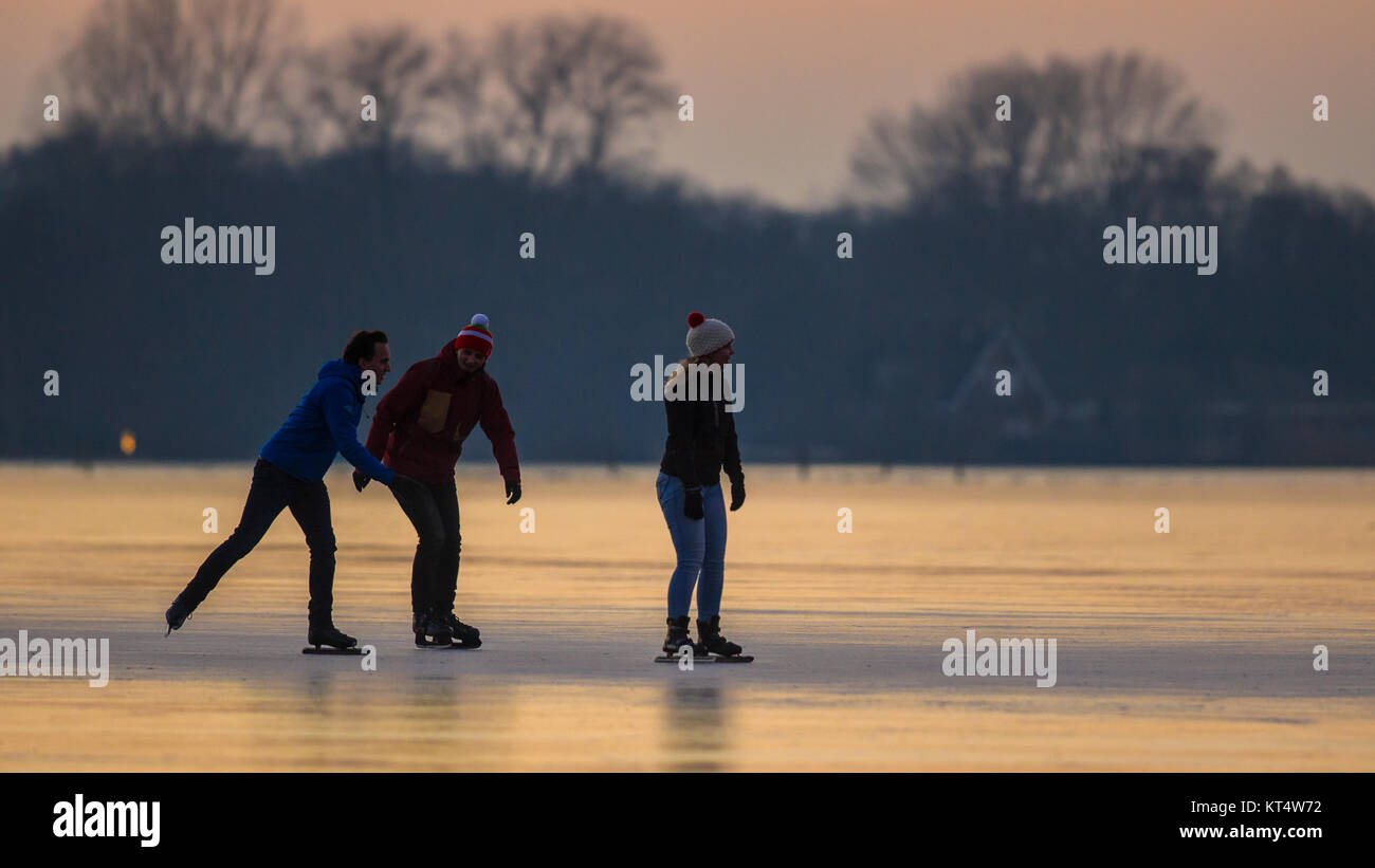 GRONINGEN, THE NETHERLANDS - JANUARY 26, 2017: People are Ice speed skating like silhouettes in orange light of setting sun on frozen lake in the Neth Stock Photo