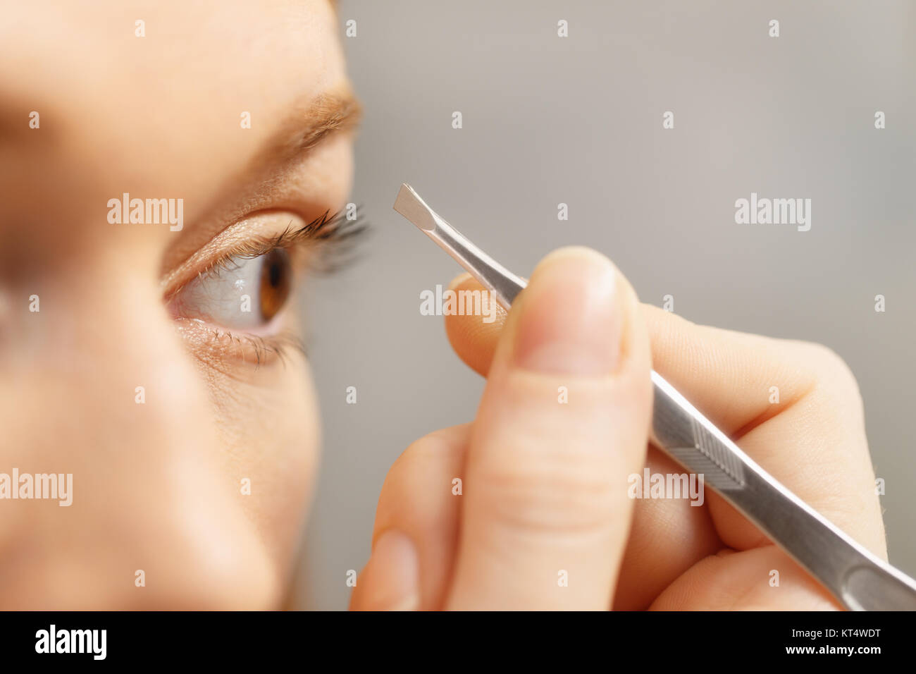 Girl pulling eyebrows with tweezers. Young woman looking at mirror