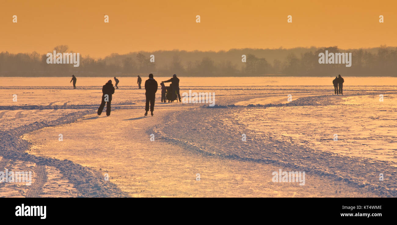Dutch Ice Skaters on frozen lake seen on their back under orange sunset Stock Photo