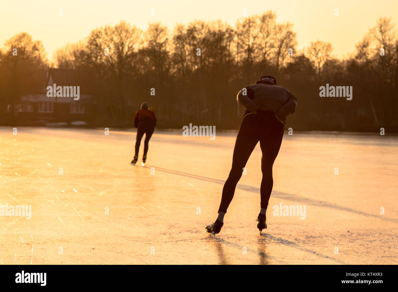 Ice speed skating silhouettes in orange light of setting sun on frozen lake in the Netherlands Stock Photo