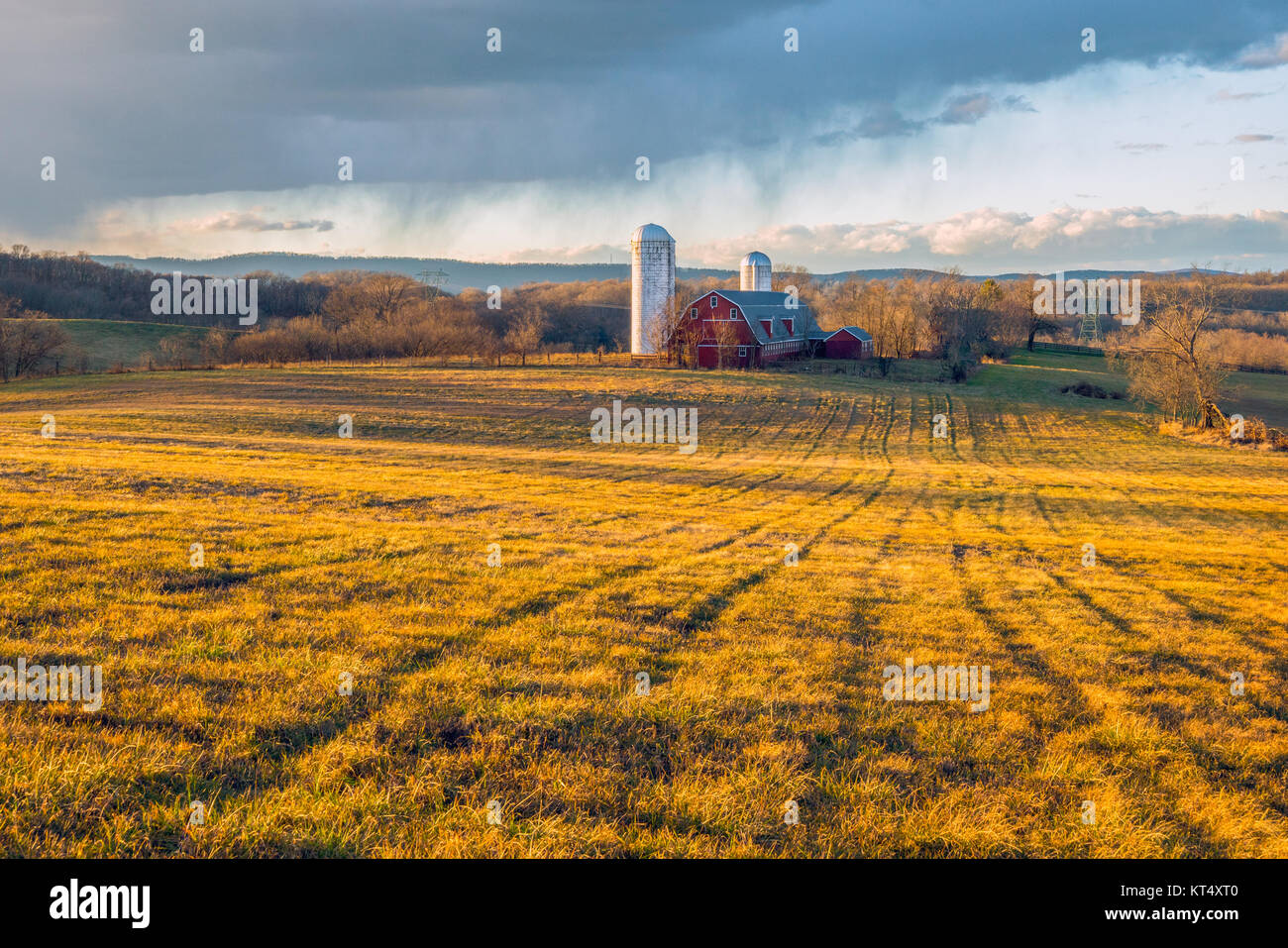 Late afternoon sunshine sprays and casts shadows across a farm field as a cold winter day comes to an end. Stock Photo