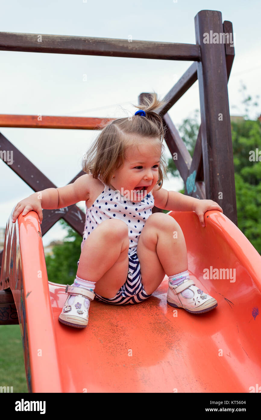 smiling girl sliding down on slide at playground Stock Photo