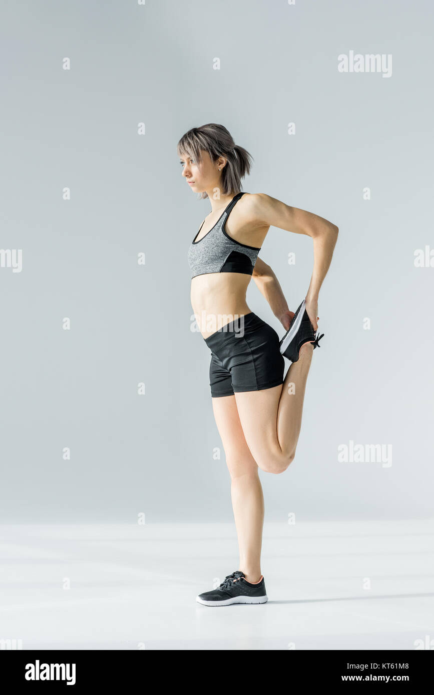 Side view of young athletic woman in sportswear exercising on grey ...