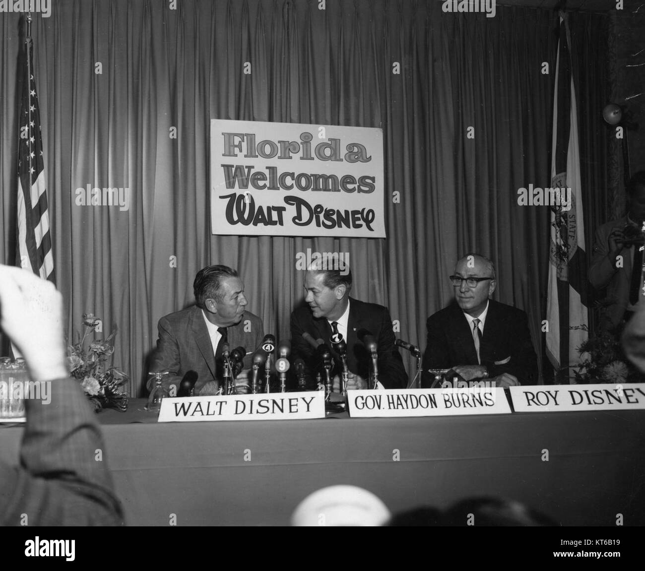 Walt Disney is pictured with his company at a press conference. The image captures the legendary entertainment mogul engaging with the media in a professional setting. Stock Photo