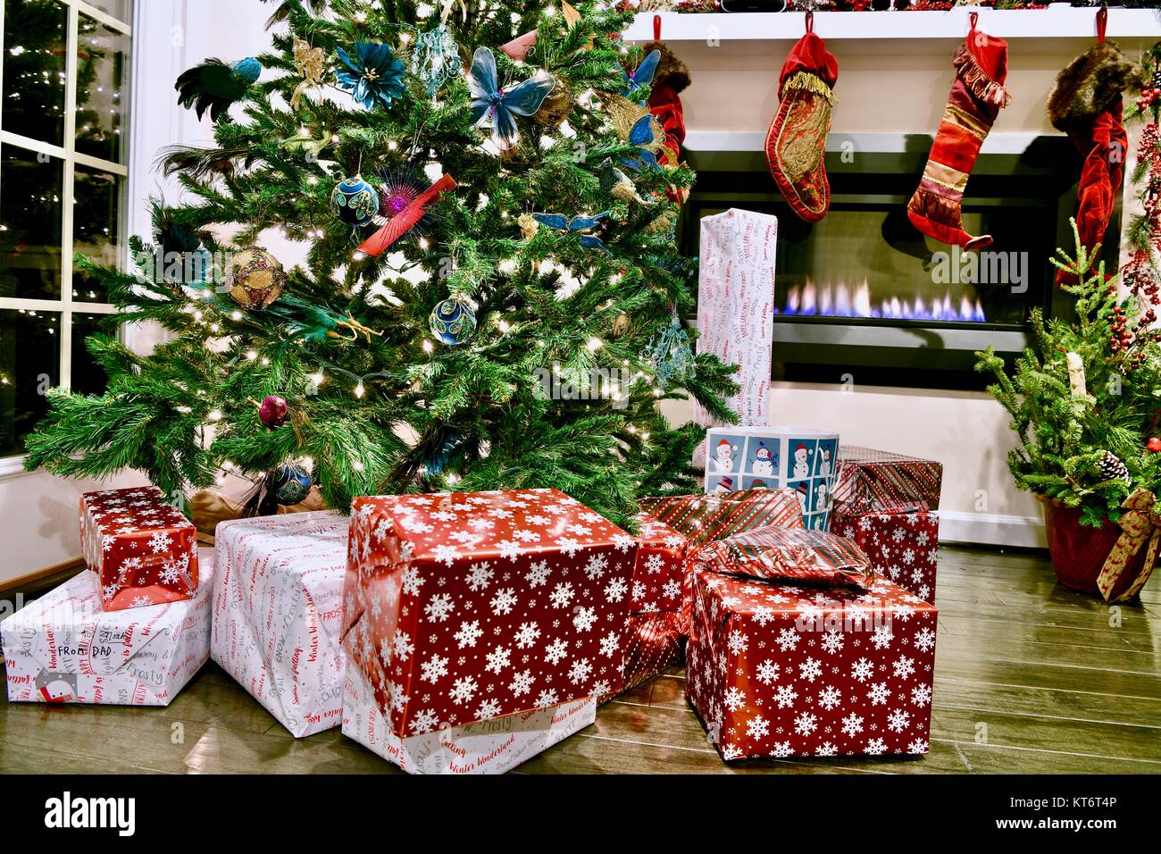 Christmas tree full of ornaments and lights with wrapped presents underneath next to a cozy gas