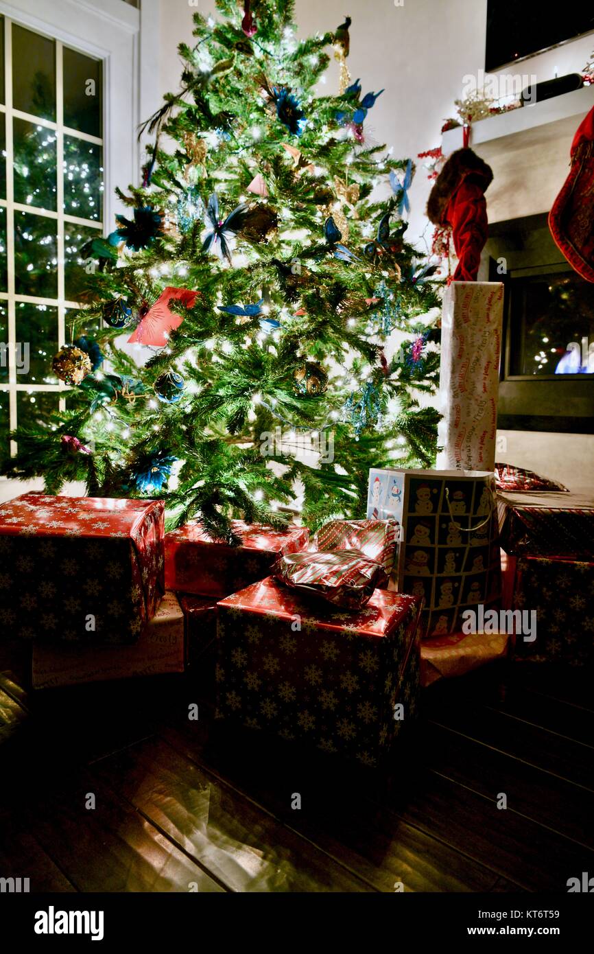 Christmas tree full of ornaments and lights with wrapped presents underneath next to a cozy gas