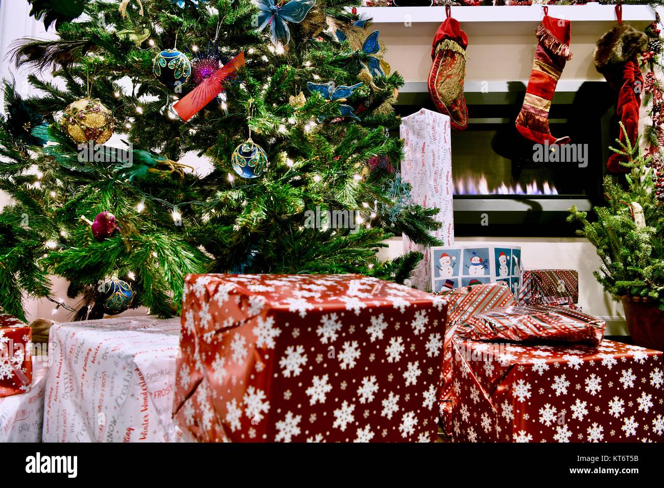 Christmas tree full of ornaments and lights with wrapped presents underneath next to a cozy gas
