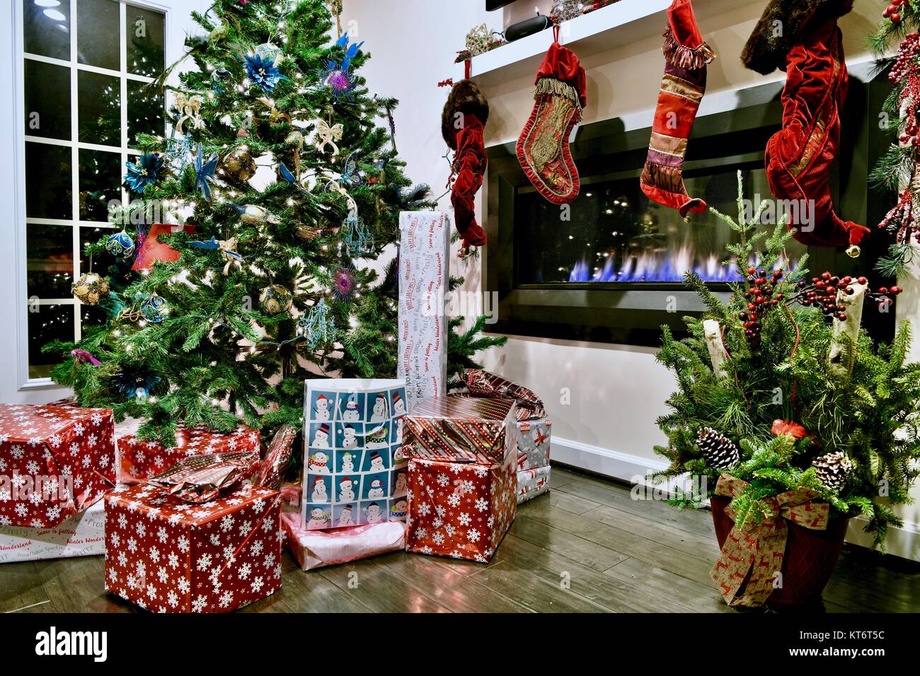 Christmas tree full of ornaments and lights with wrapped presents underneath next to a cozy gas
