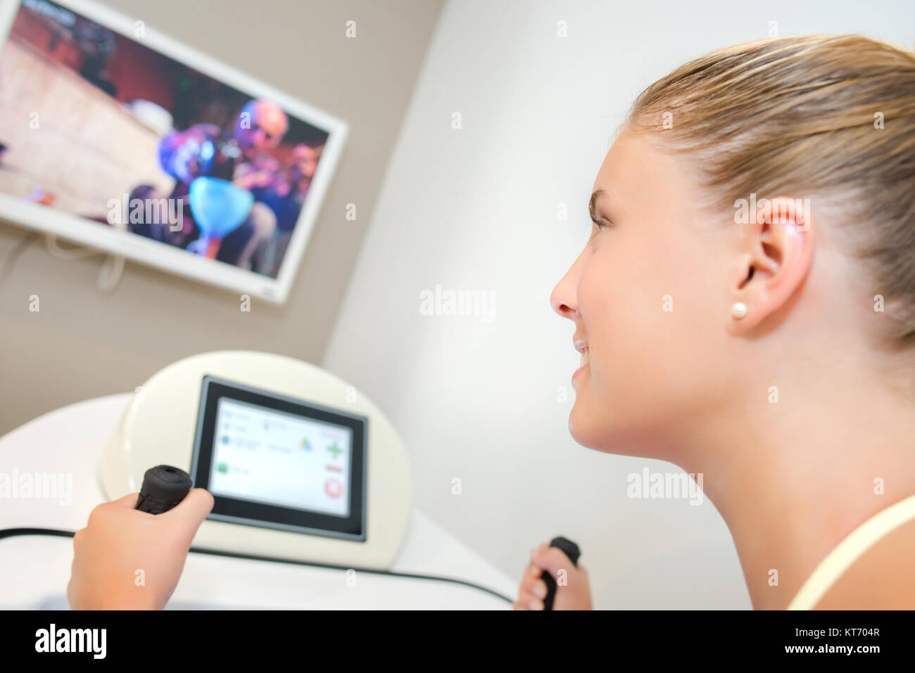 Lady on exercise machine, watching TV screen Stock Photo