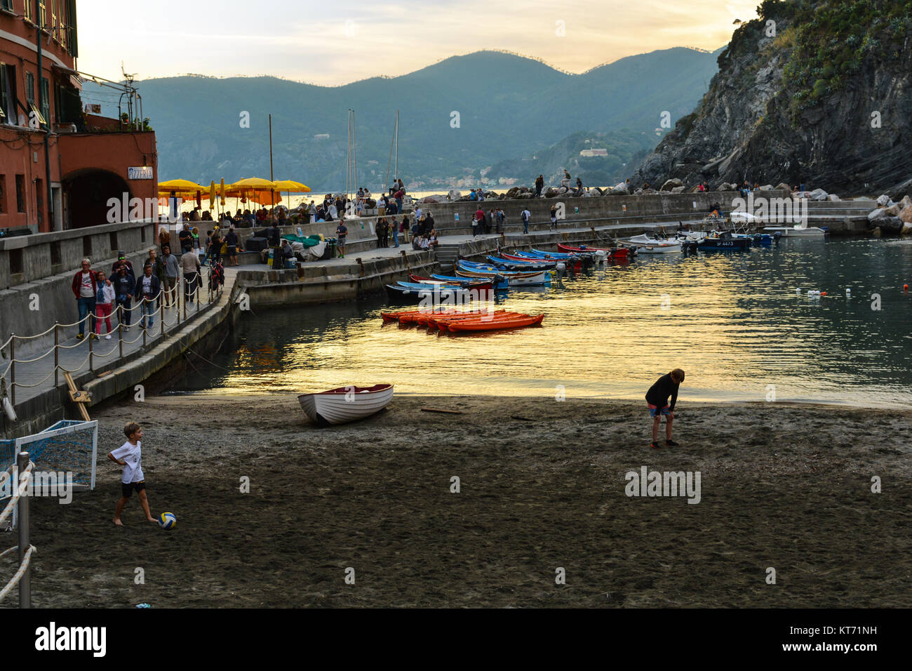 Local Italian children play football on the sandy beach at Vernazza as tourists watch at dusk along the Cinque Terre coast of Italy Stock Photo