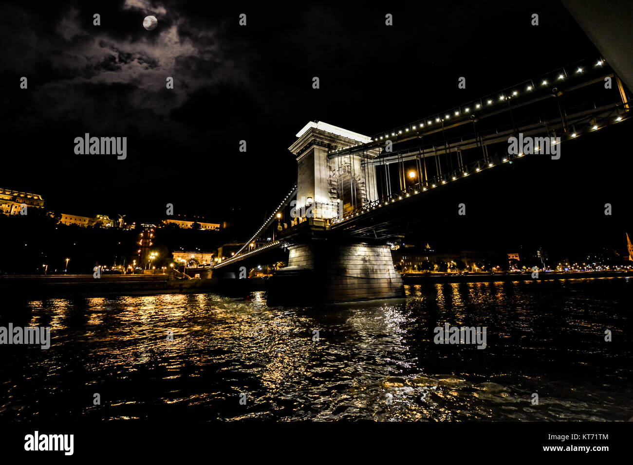 City lights of Budapest from the Danube River under a full moon and with the Chain Bridge lit up at night Stock Photo