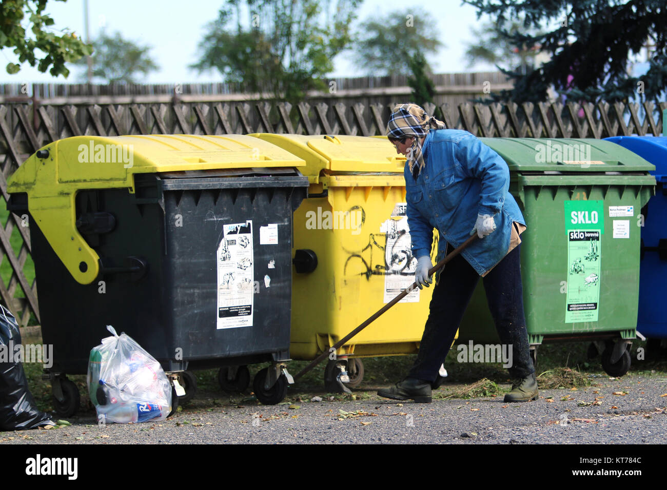 woman sweeping in front of garbage bins Stock Photo Alamy