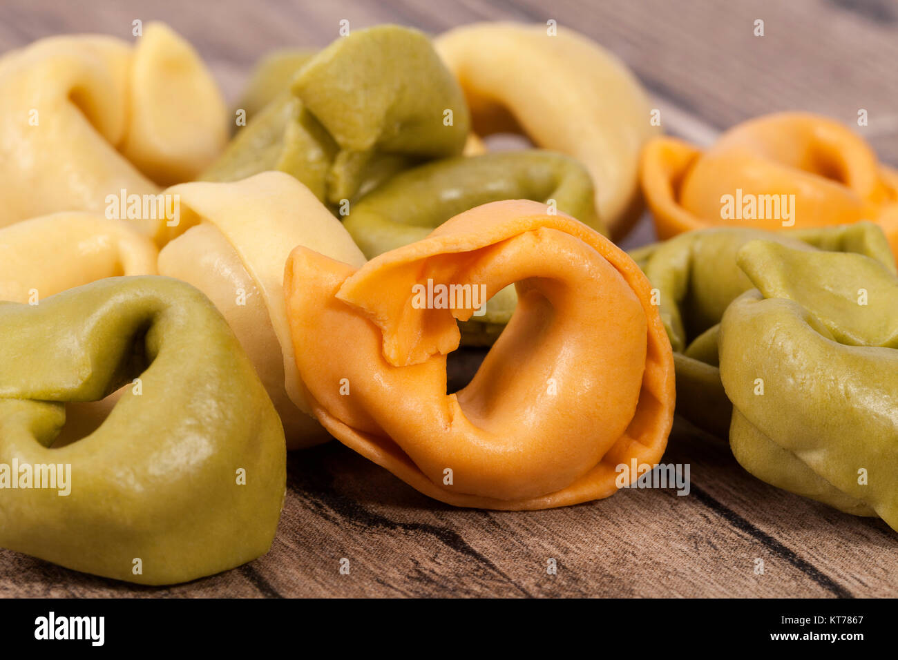Colored tortellini, ring-shaped pasta on wooden plank Stock Photo