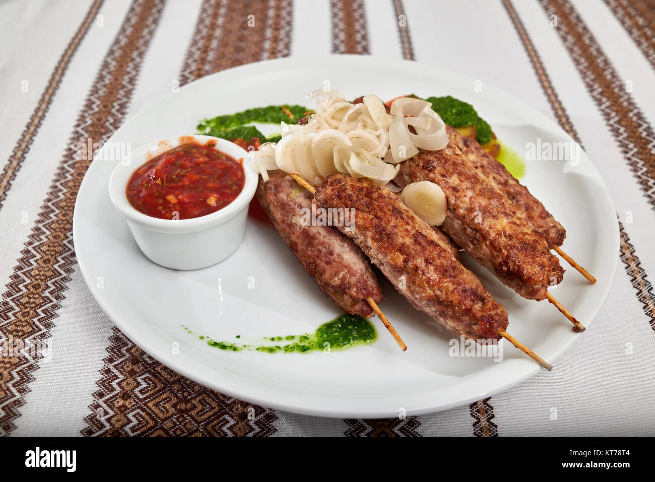 Delicious restauranr appetizer for beer and hard alcohol: roasted sausage set with tomato and green sauce and onion slices. A table is covered with em Stock Photo