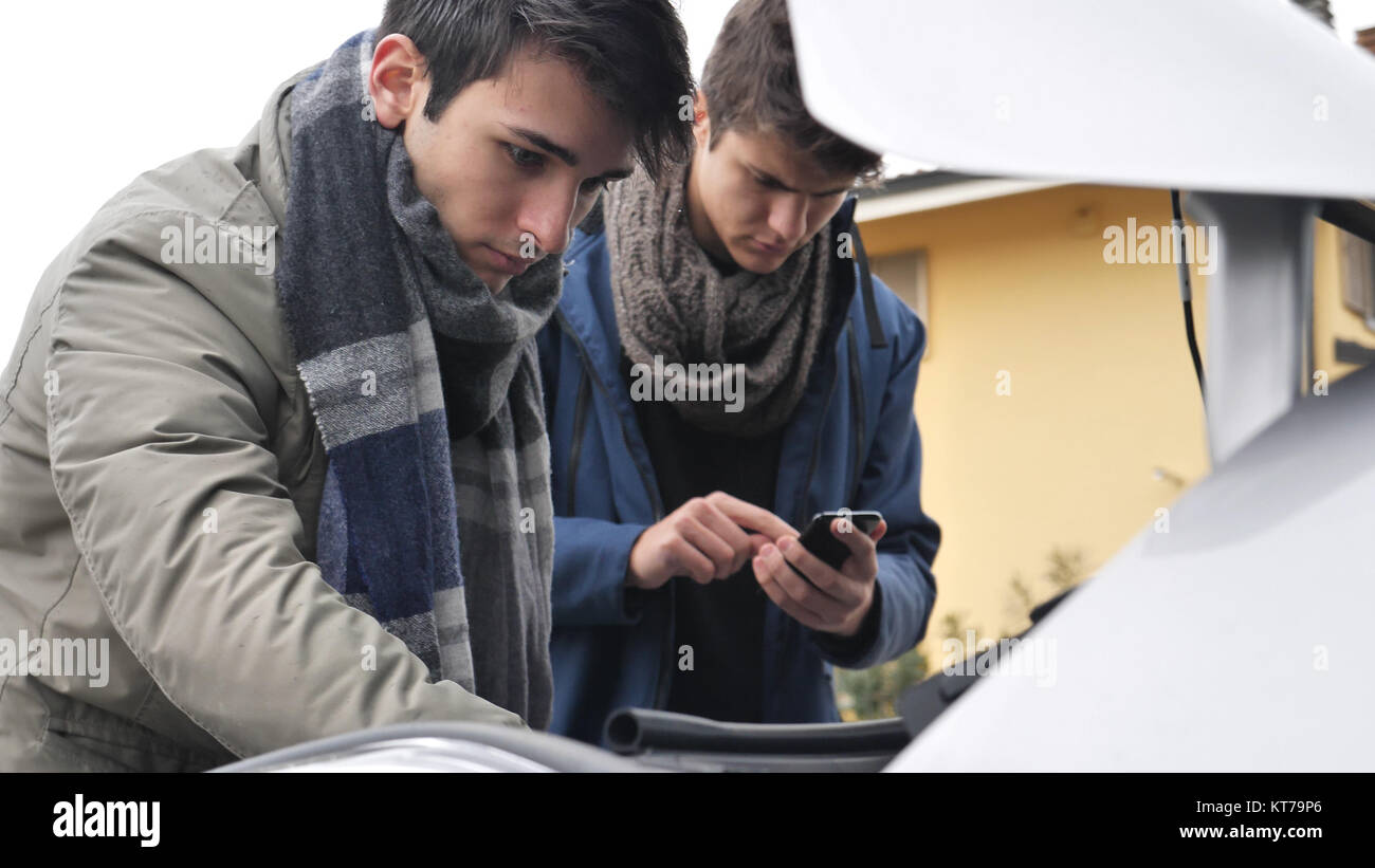 Young men looking up information while trying to repair car engine ...