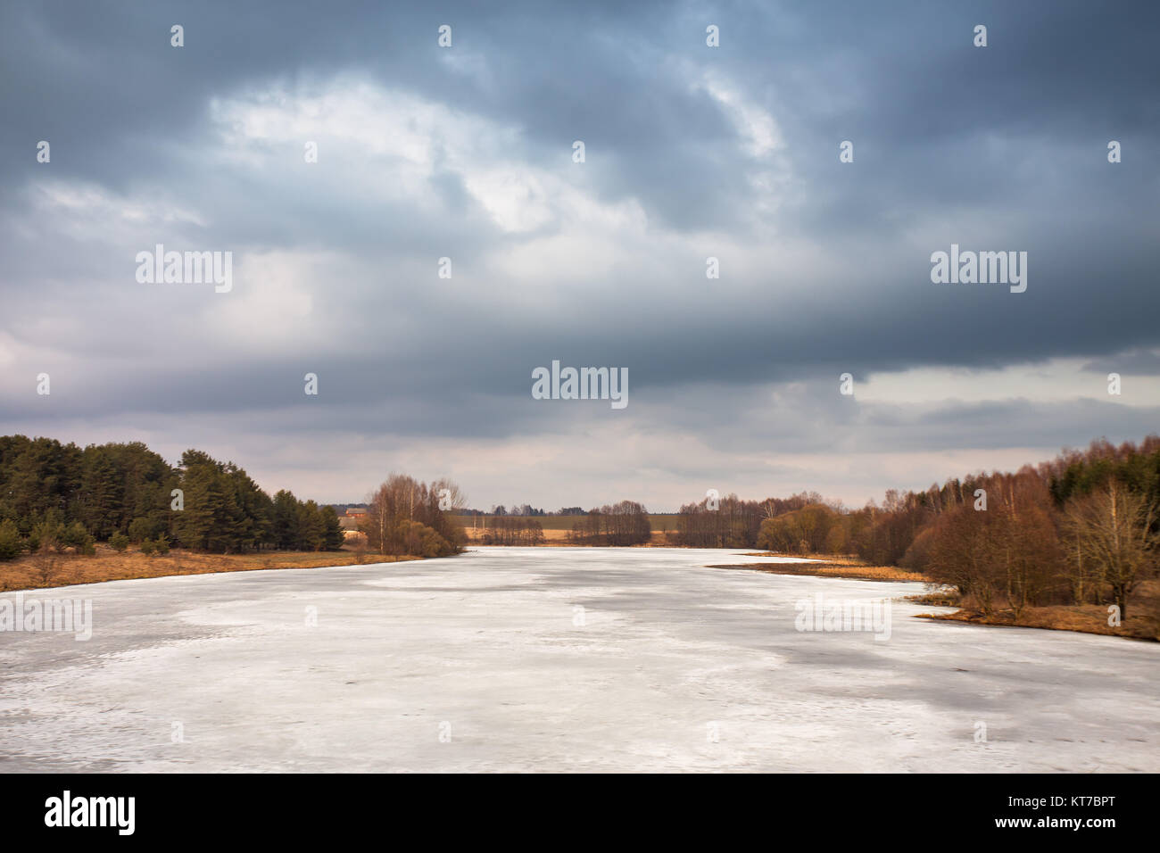 Spring rural scene. Lake under ice and snow melting. Cloudy spring day Stock Photo