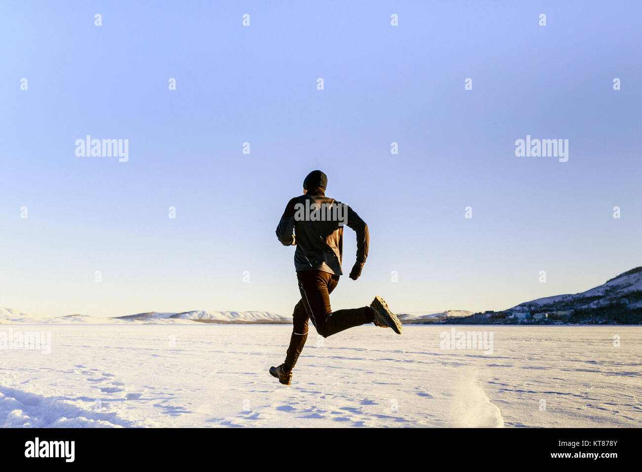 rear view athlete runner running on snow in black sport clothes Stock Photo