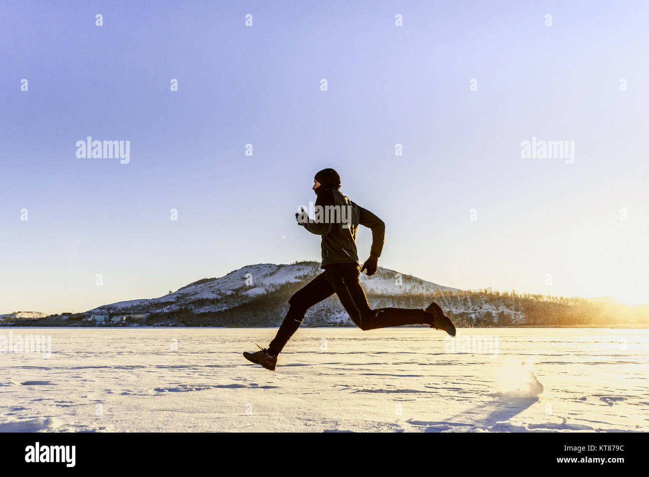 winter running in snow male runner in background of mountain and sun Stock Photo