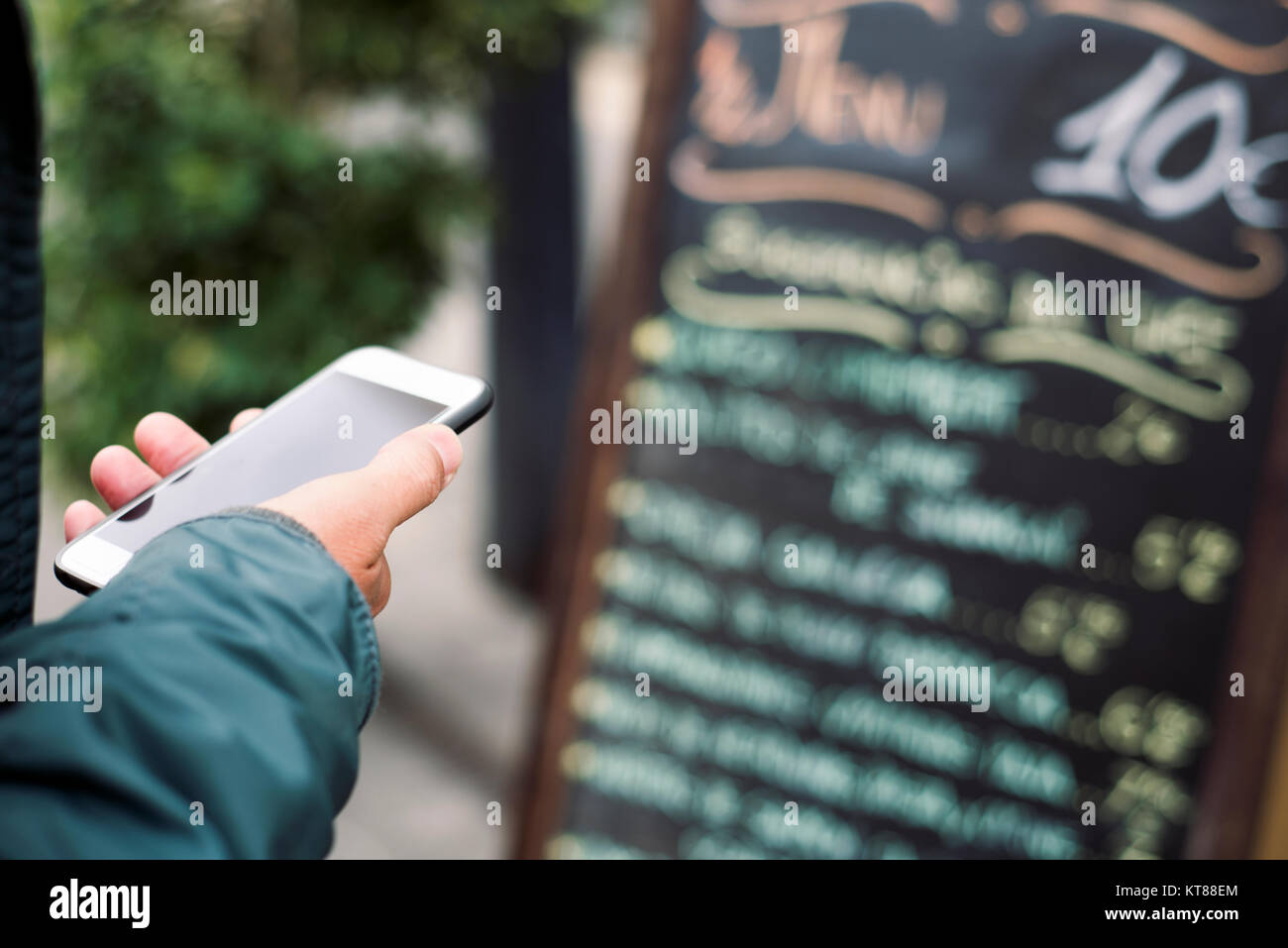 closeup of a young caucasian man using a smartphone in the street, in front of a restaurant, reading the online reviews of the premises or reserving a Stock Photo