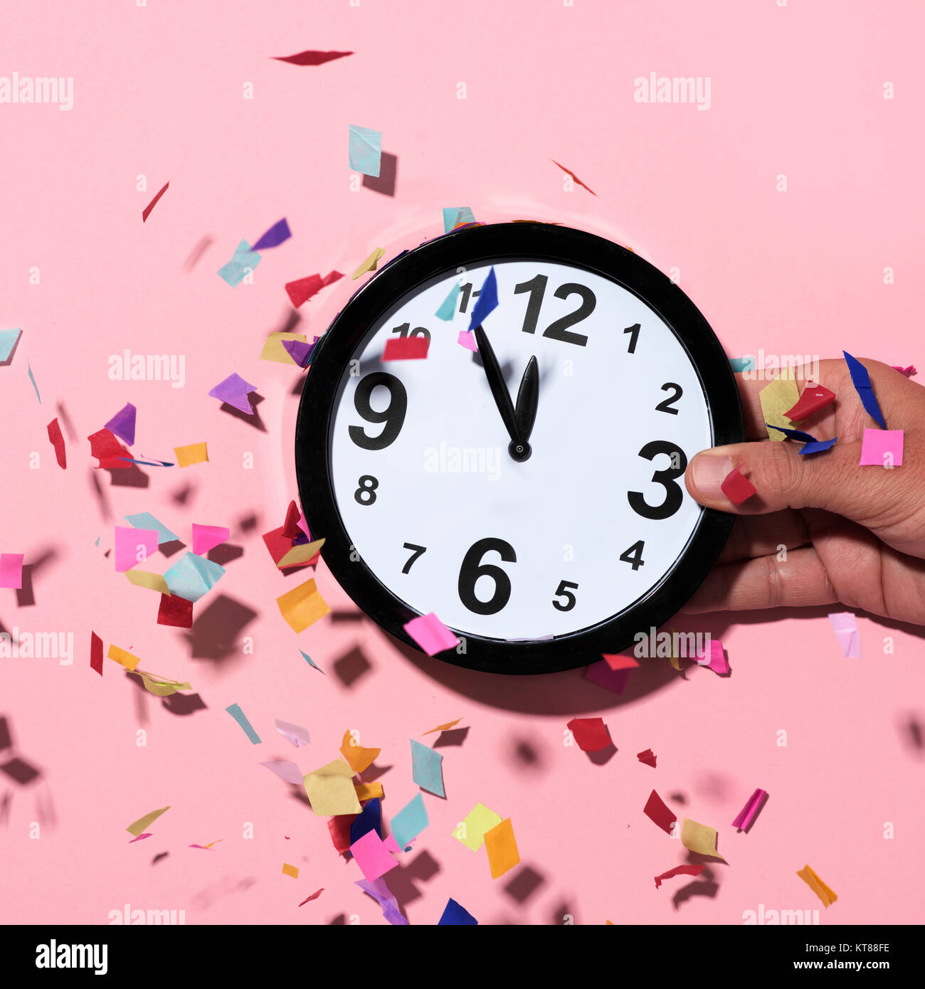 confetti of different colors falling over a clock at five to twelve in the hand of a young man