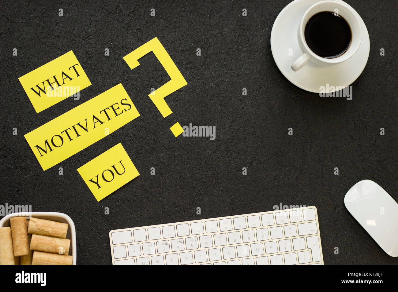 What motivates you question printed on a yellow paper with coffee, cookies and office items. Black concrete background. Business and management concep Stock Photo