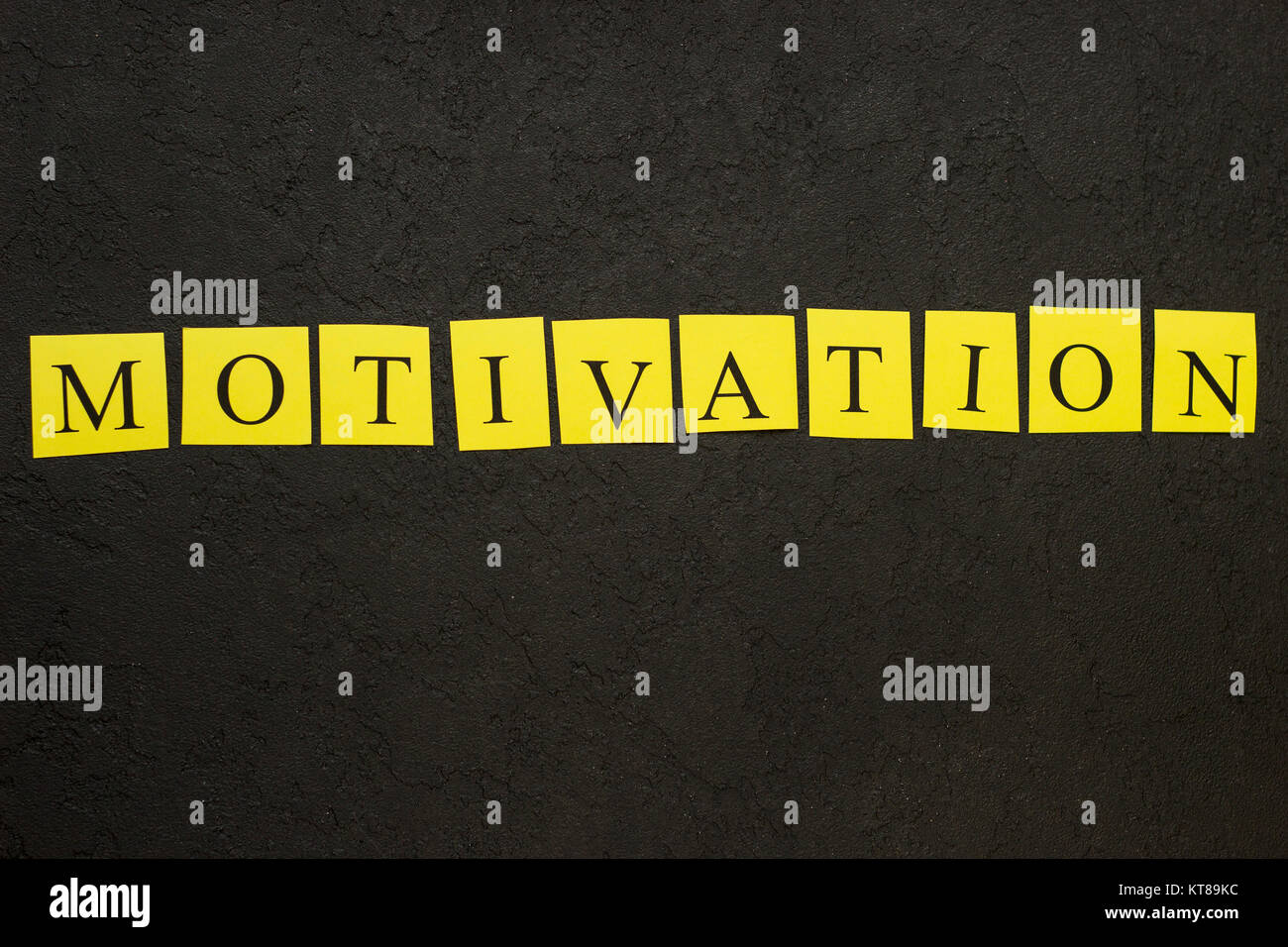 Motivation horizontal inscription of letters printed on yellow papers. Black concrete background. Space for your text or product display. Top view. Stock Photo