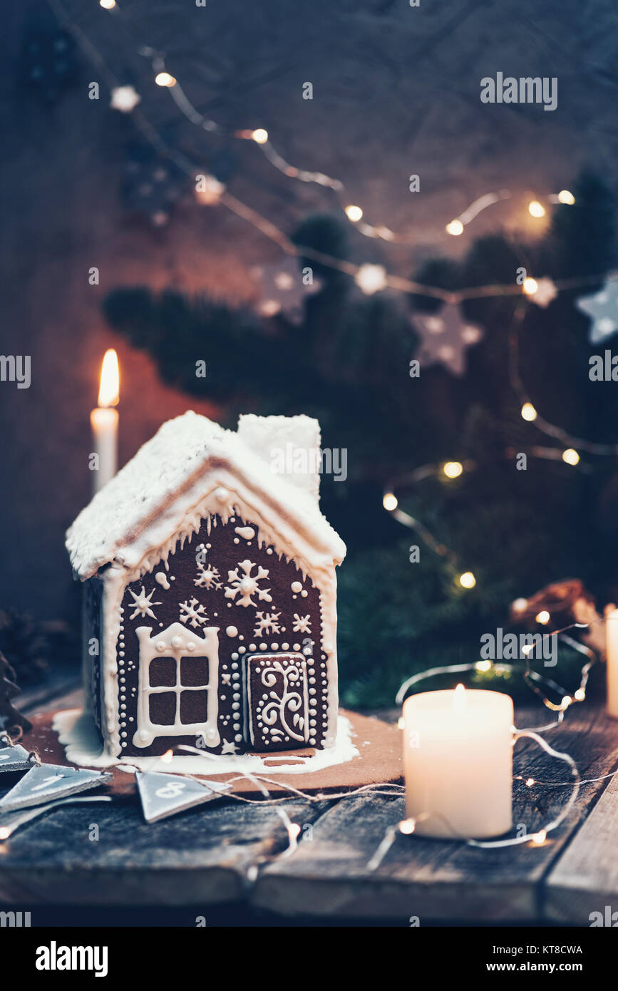 Gingerbread house, candles, Christmas lights and fir tree. Moody winter