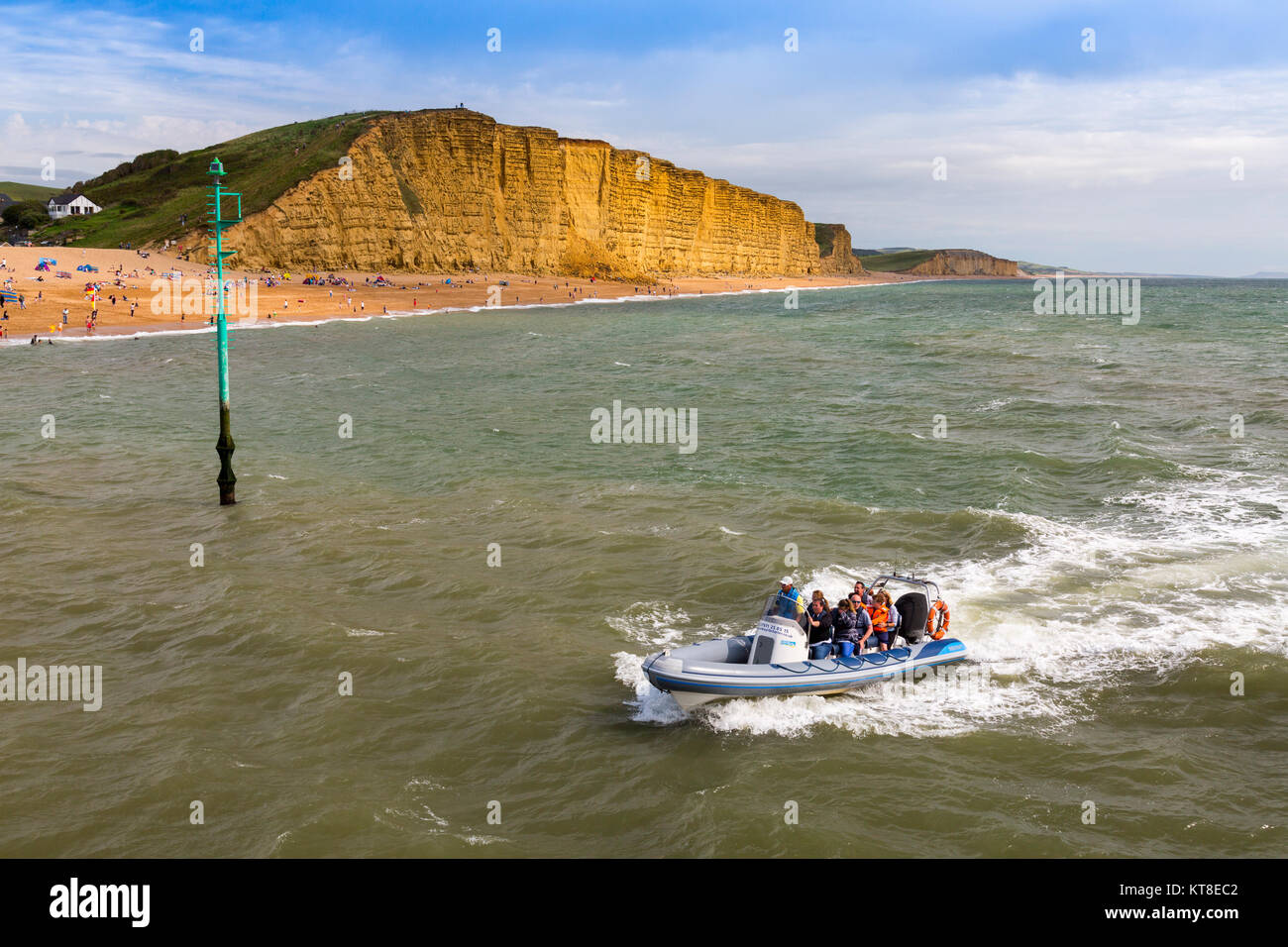 An inflatable rib full of tourists approaches the entrance to West Bay harbour in front of East Cliff on the Jurassic Coast, Dorset, England, UK Stock Photo