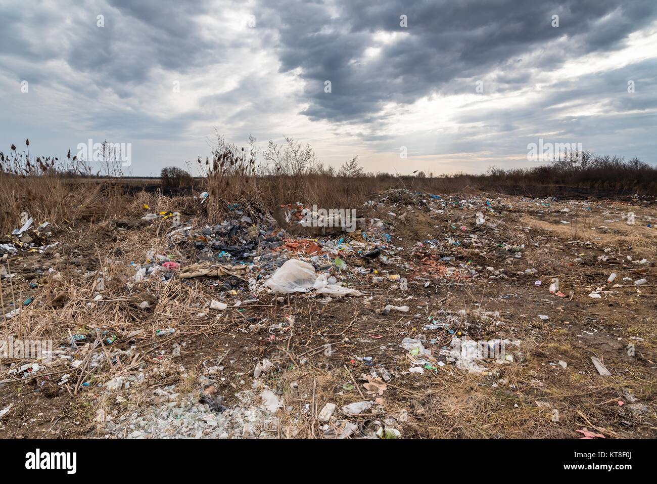 Rubbish pollution with plastic and other packaging stuffs in the nature with dramatic cloudy sky. The demonstration of environmental problems. Stock Photo