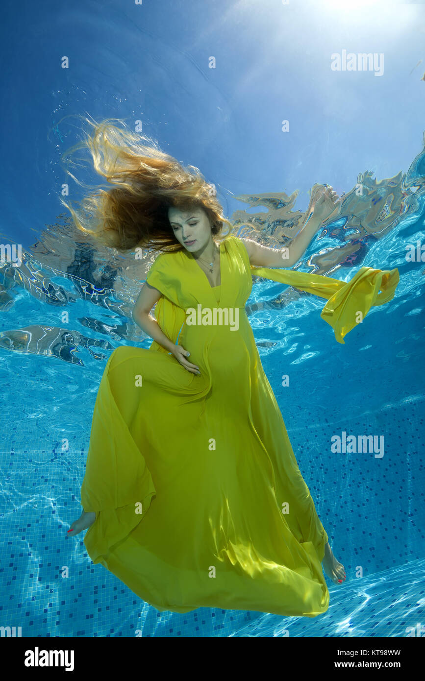 Young pregnant woman in yelow dress under water in the pool Stock Photo
