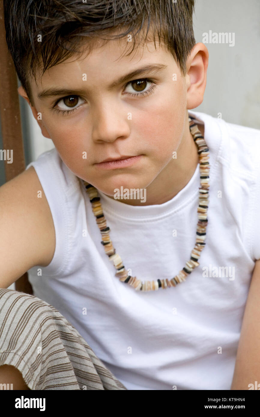 Fashion. Cute little boy looking at the camera, wearing a white tshirt and a necklace Stock Photo