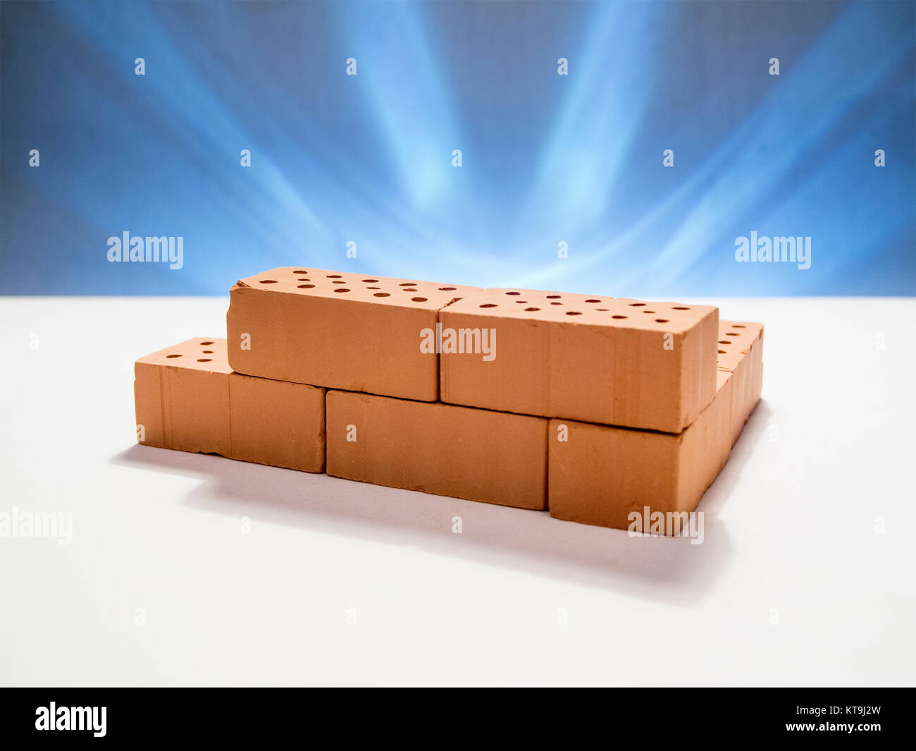 angedeutetes Mauerwerk aus Spielzeug-Ziegelsteinen auf weißen Hintergrund vor sternförmig blau beleuchteten Hintergrund Stock Photo
