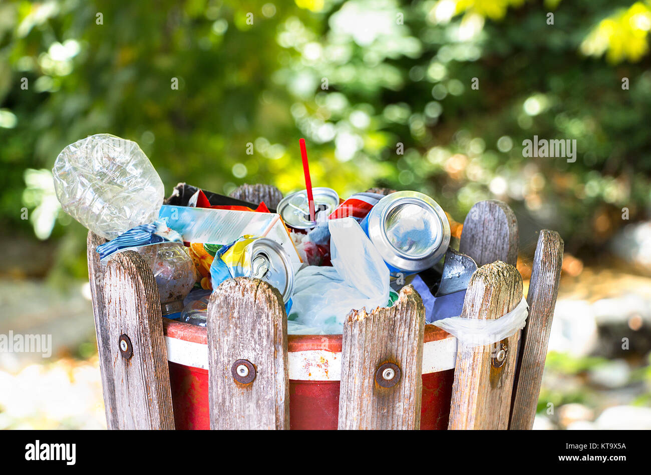 A wooden garbage bin outside in a park full with plastic bottles, cans, paper and plastic bags. Stock Photo