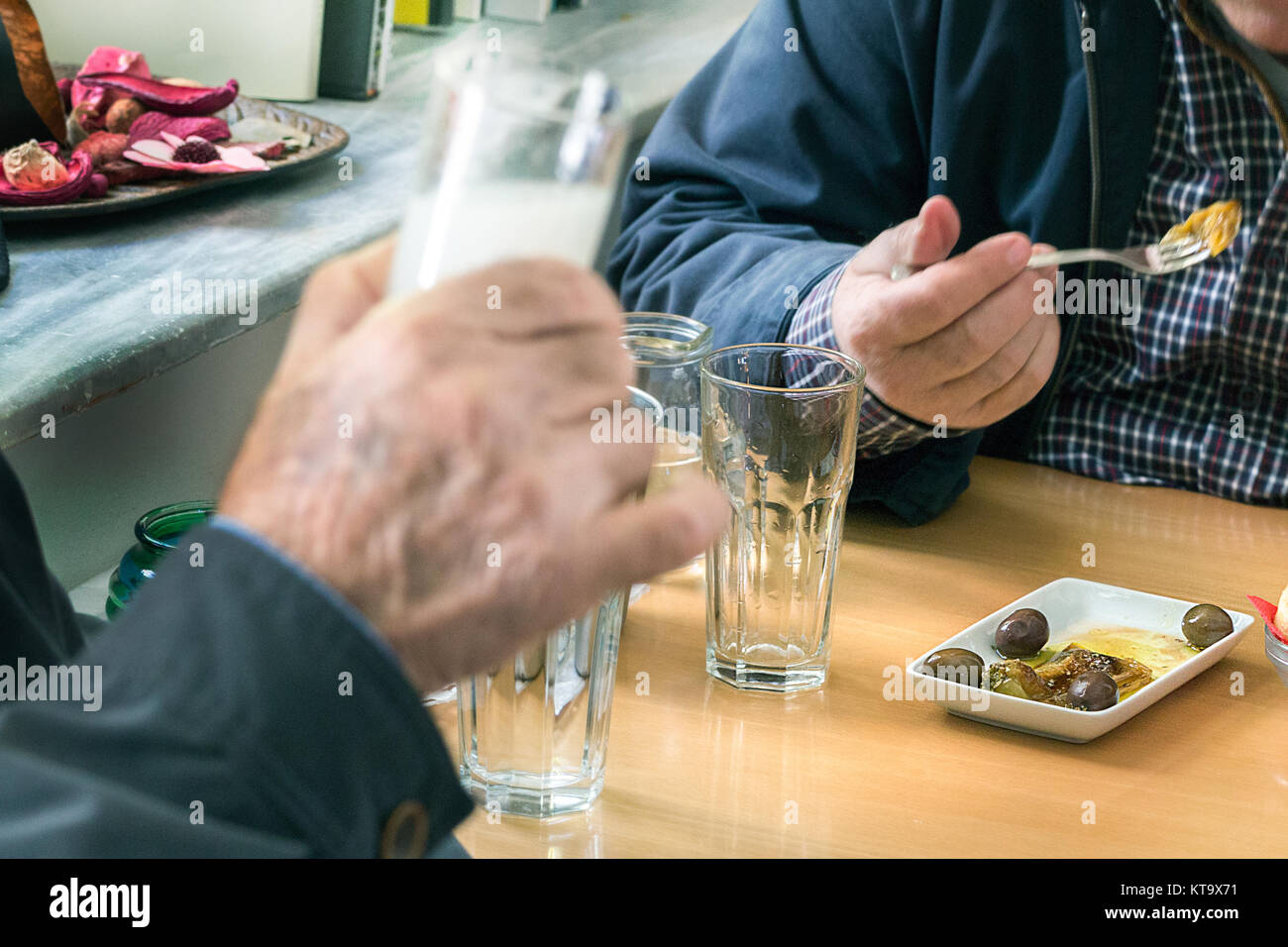 Two customers drinking ouzo with olives (mezedes) inside a traditional Ouzeri Greek tavern. Stock Photo