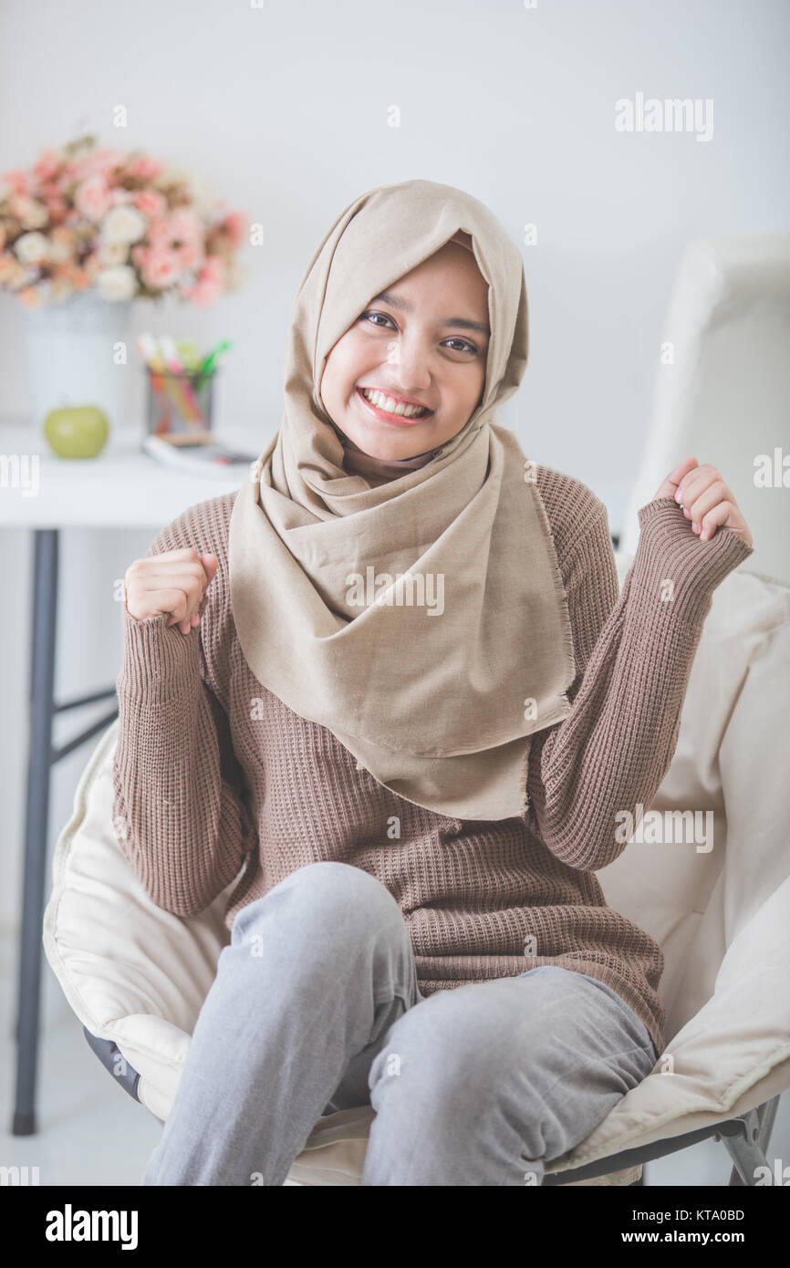 portrait of excited young woman with hijab smiling while sitting on a ...