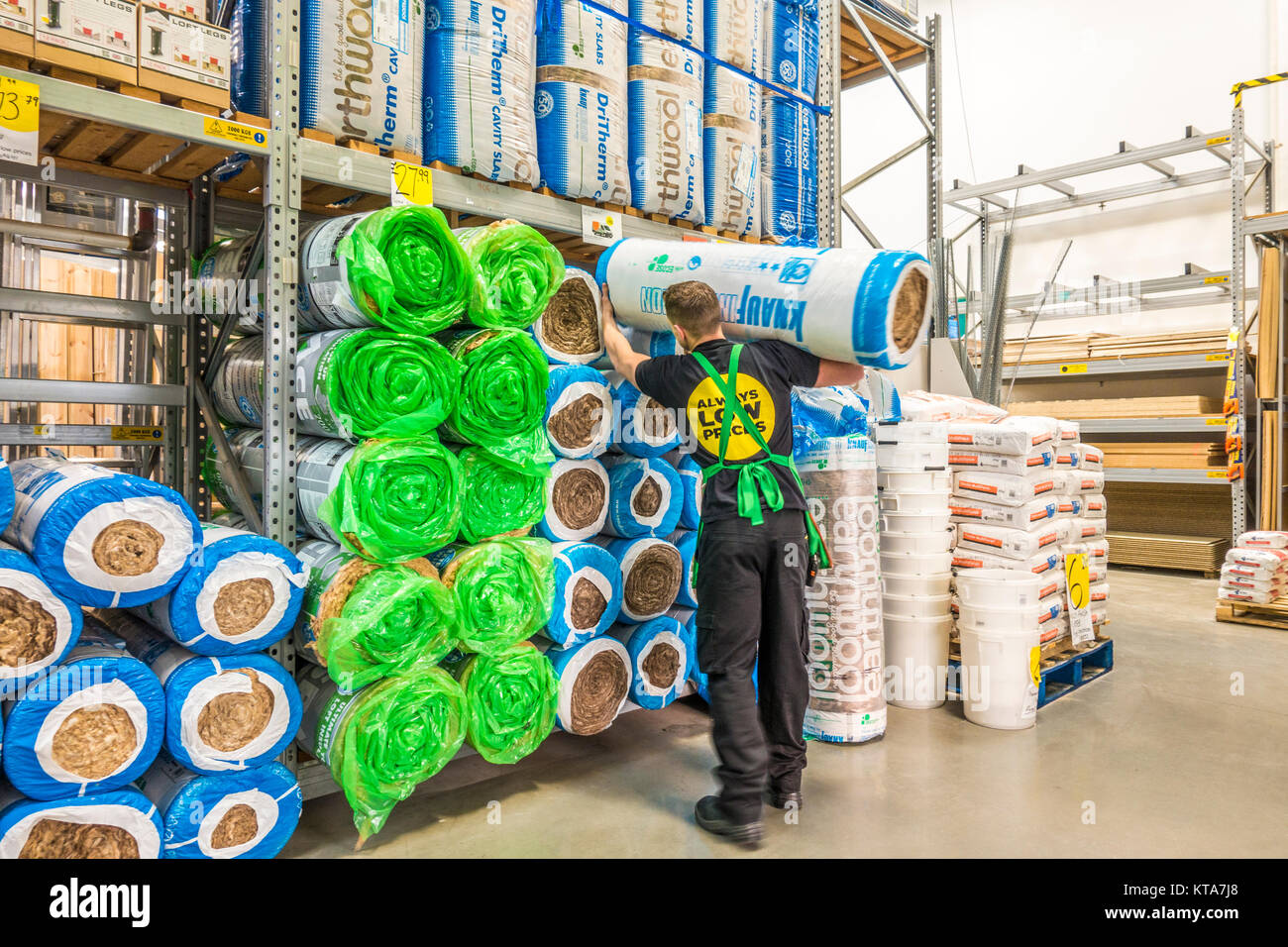 Young male employee standing and holding a large roll of Knauf insulation, placing it on a rack, in a Homebase DIY store. Stamford, England, UK. Stock Photo