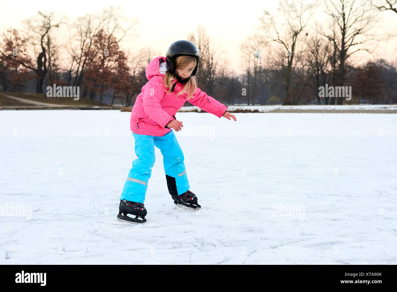 Child girl falling down on ice in snowy park during winter holidays. Wearing safety helmet. Winter children activities. Stock Photo