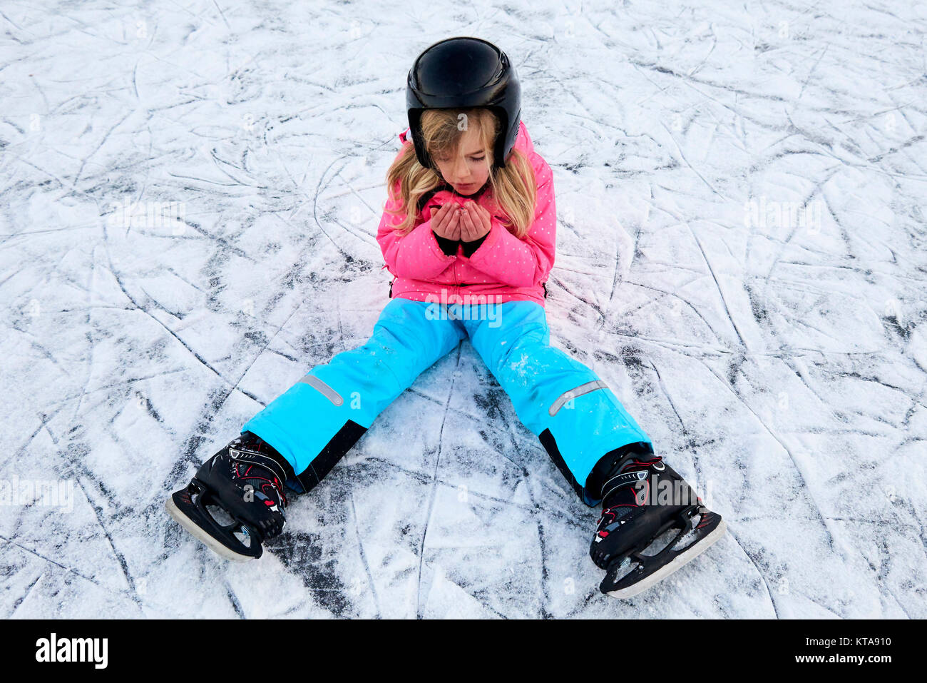 Child girl falling down on ice in snowy park during winter holidays. Wearing safety helmet. Winter children activities. Stock Photo