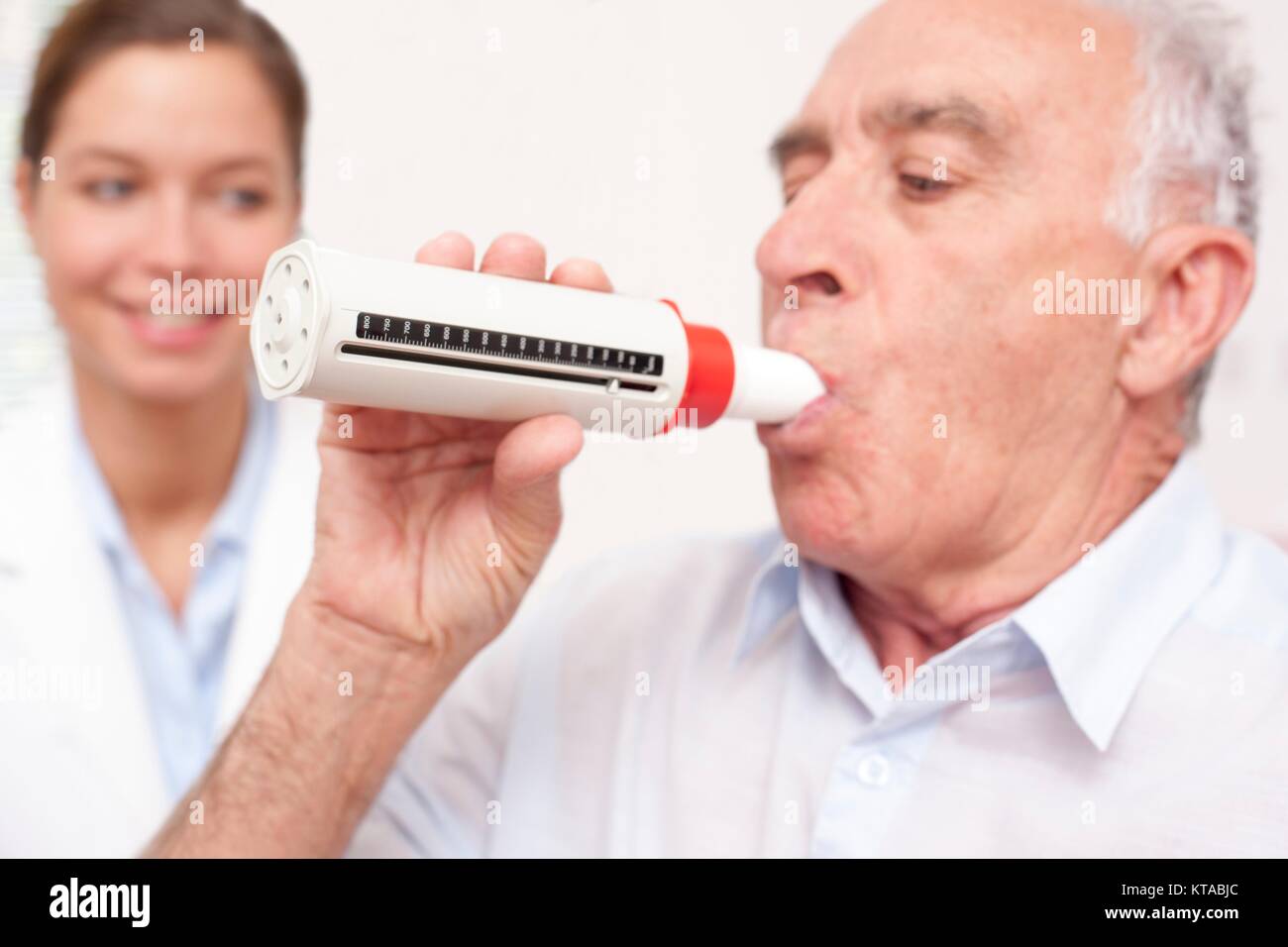 Senior man exhaling into a peakflow reader, nurse watching. Stock Photo