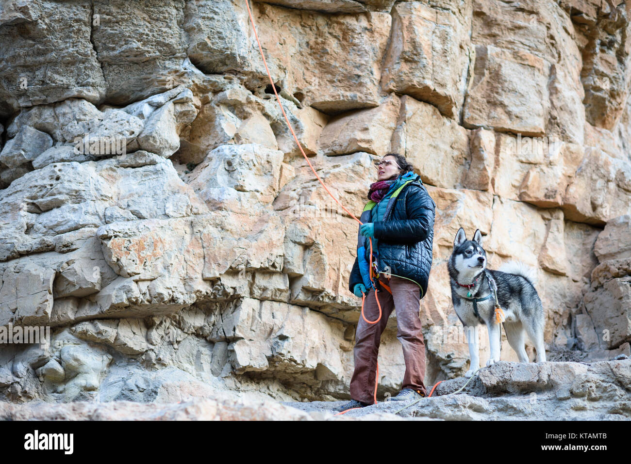 Outdoor sport activity. Professional rock climber Alizée Dufraisse belaying another person on a challenging cliff. Faithful husky dog waiting for his  Stock Photo