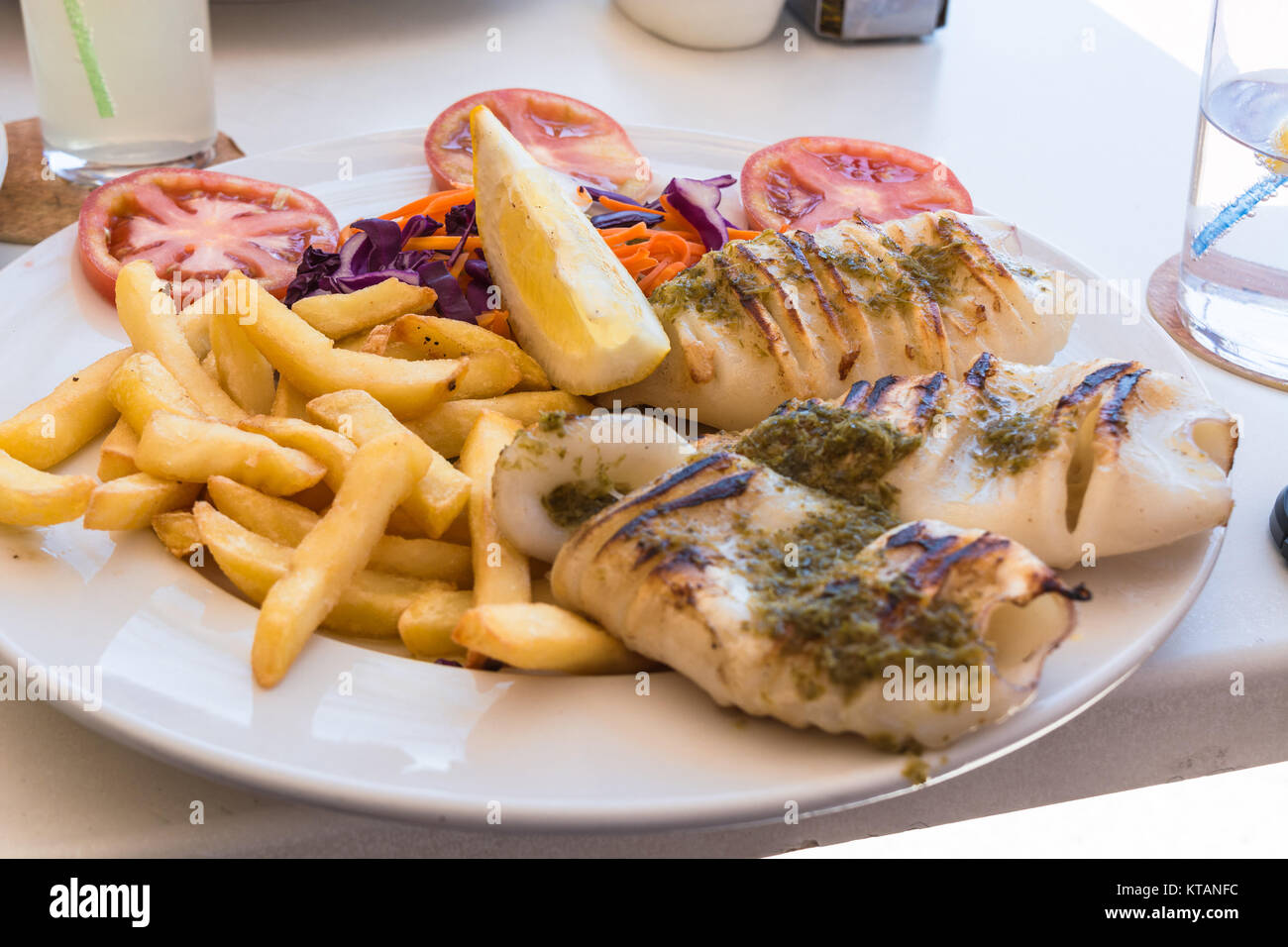 Gegrillten Oktopus. Gegrillter Tintenfisch serviert mit Pommes frittes und Zitronen und Salat. Stock Photo