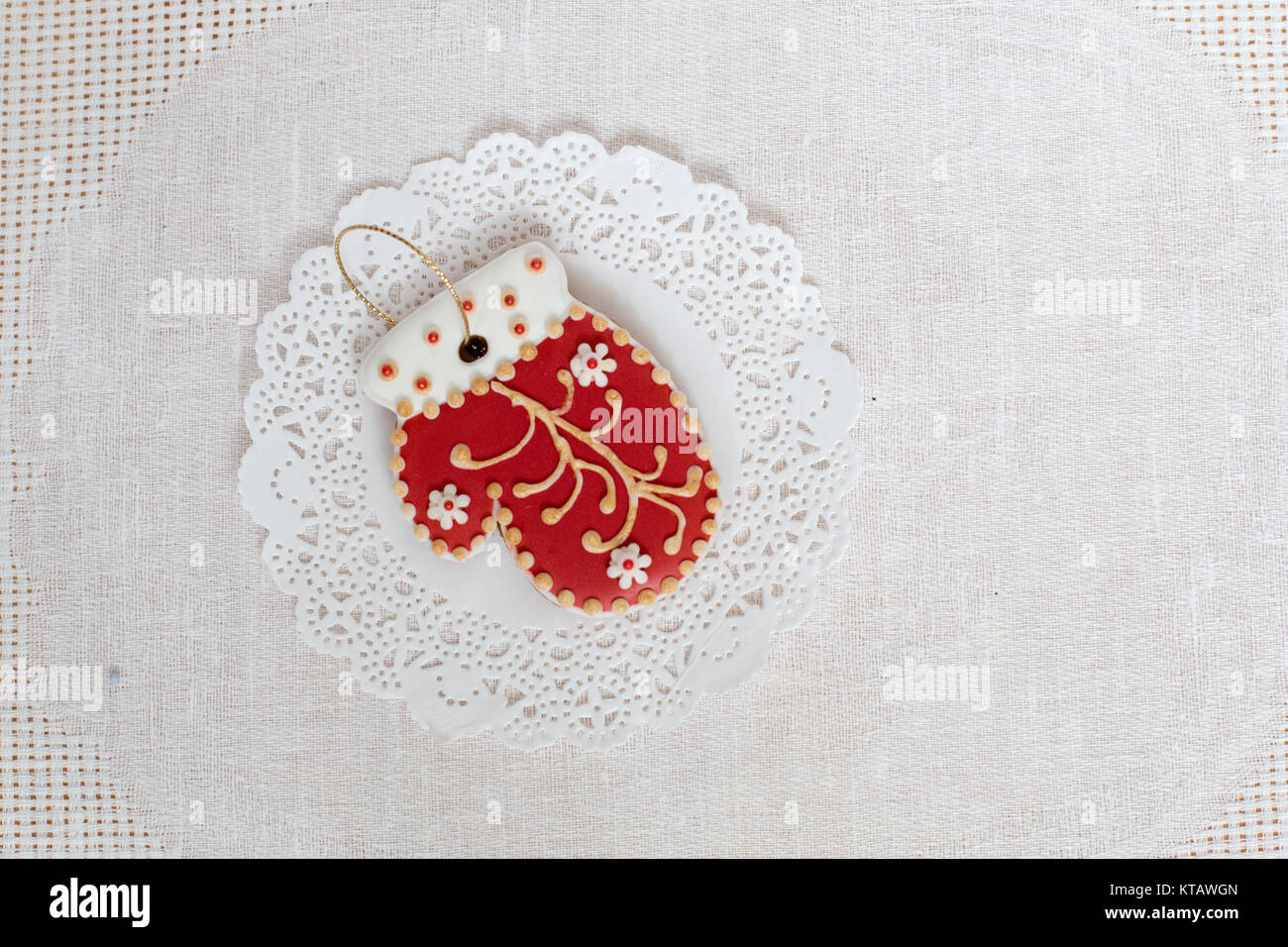 Gingerbread cookie in the shape of red mitten on a white napkin background. Top view, flat lay, copy space. Curly Christmas gingerbread home cooking.  Stock Photo