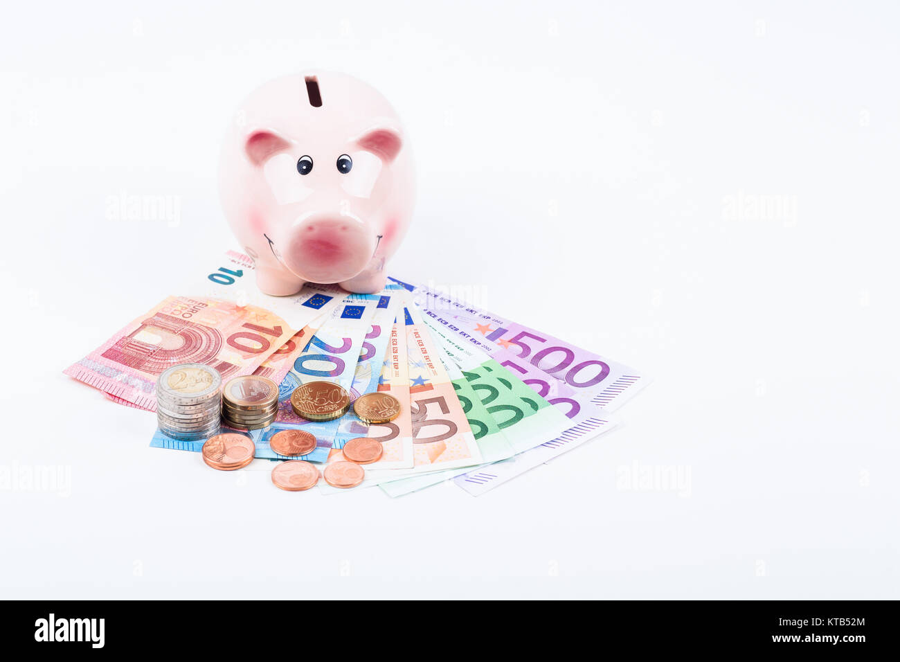 Sparschwein mit Geldscheinen und Münzen auf weisser Fläche Stock Photo