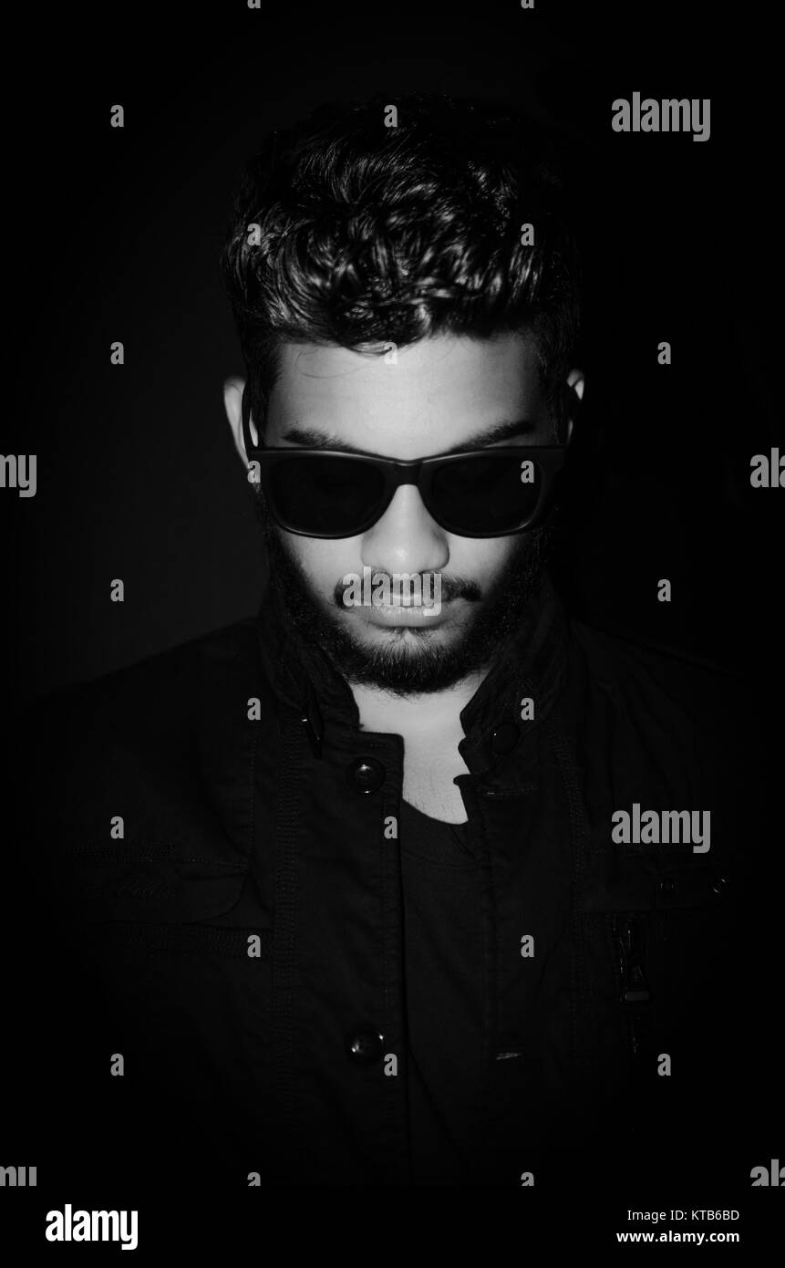 Black and white portrait of a stylish young man wearing sunglasses on a black background. Stock Photo
