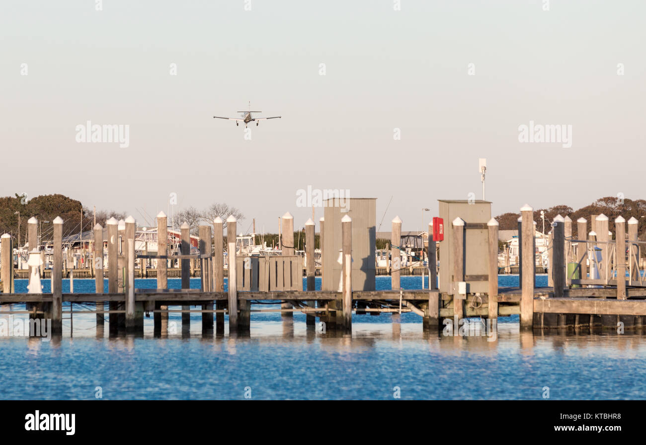 small single engine plane on an approach to montauk's airport, flying over a marina Stock Photo